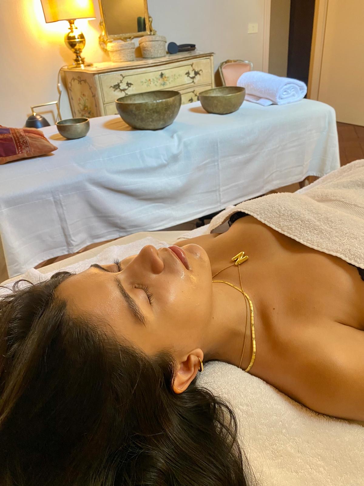 Cliente rilassata sul lettino, con campane tibetane e asciugamani arrotolati sullo sfondo