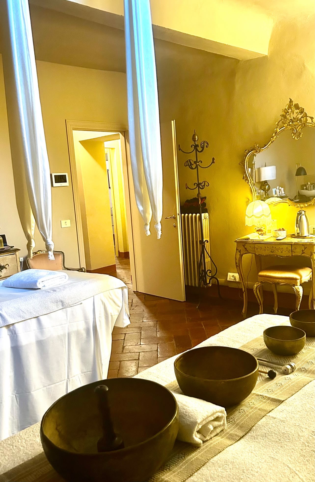 Sala dei trattamenti con campane tibetane e teli bianchi sospesi, con la toeletta dorata sullo sfondo